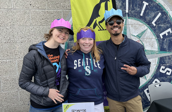 three people smiling at the camera in front of the mariners logo