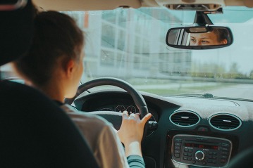 teen driving a car, eyes looking in rearview mirror