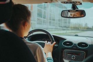 teen driving a car, eyes looking in rearview mirror