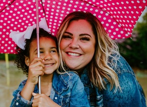 adult woman and young girl standing underneath a pink umbrella smiling in the rain