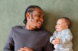 dad and baby laying on the ground looking at each other and smiling 