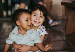 two little children sitting on the floor smiling and hugging
