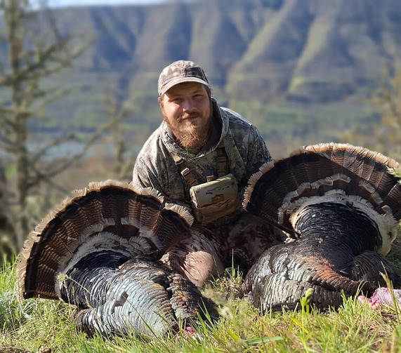 A man poses with two harvested tom turkeys