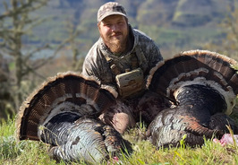 A man poses with two harvested tom turkeys