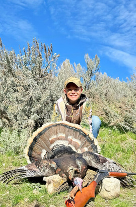 A girl stands behind a turkey she has just harvested
