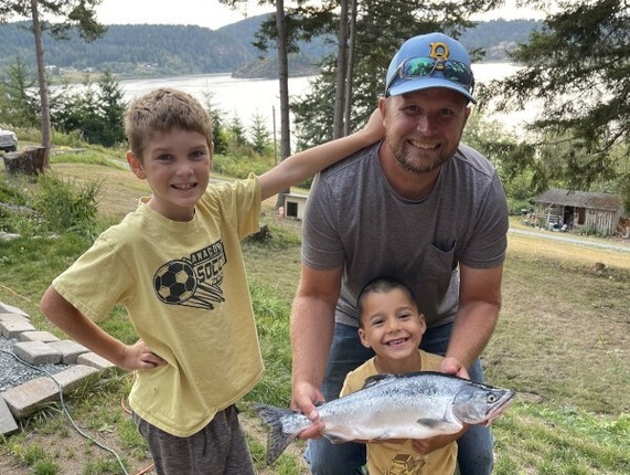 A man and two boys display a pink salmon the man has caught