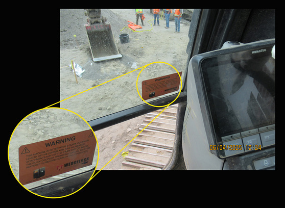 Inside view from an excavator cab showing an orange warning label on the window of the excavator.