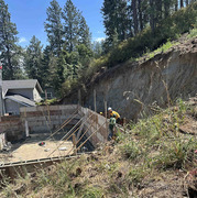 A worker is between concrete foundation blocks and next to wall of dirt. Another worker is on top of the concrete foundation blocks.