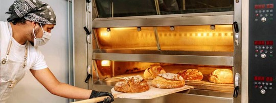 Baker putting bread in the oven in a commercial bakery
