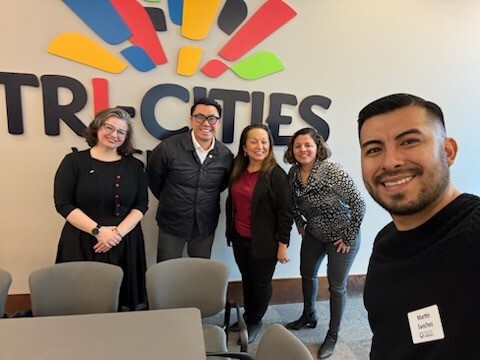 Photo of five people in front of a sign reading "Tri-Cities"