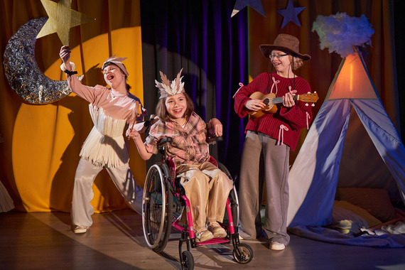 Children performing in a camp-themed stage play, including a child using a wheelchair.