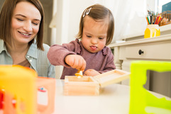 Young child playing with a wooden toy box while an adult sits nearby