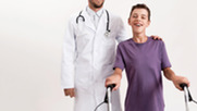 Male doctor assisting a teen boy with cerebral palsy as he walks using a walker on a white background.