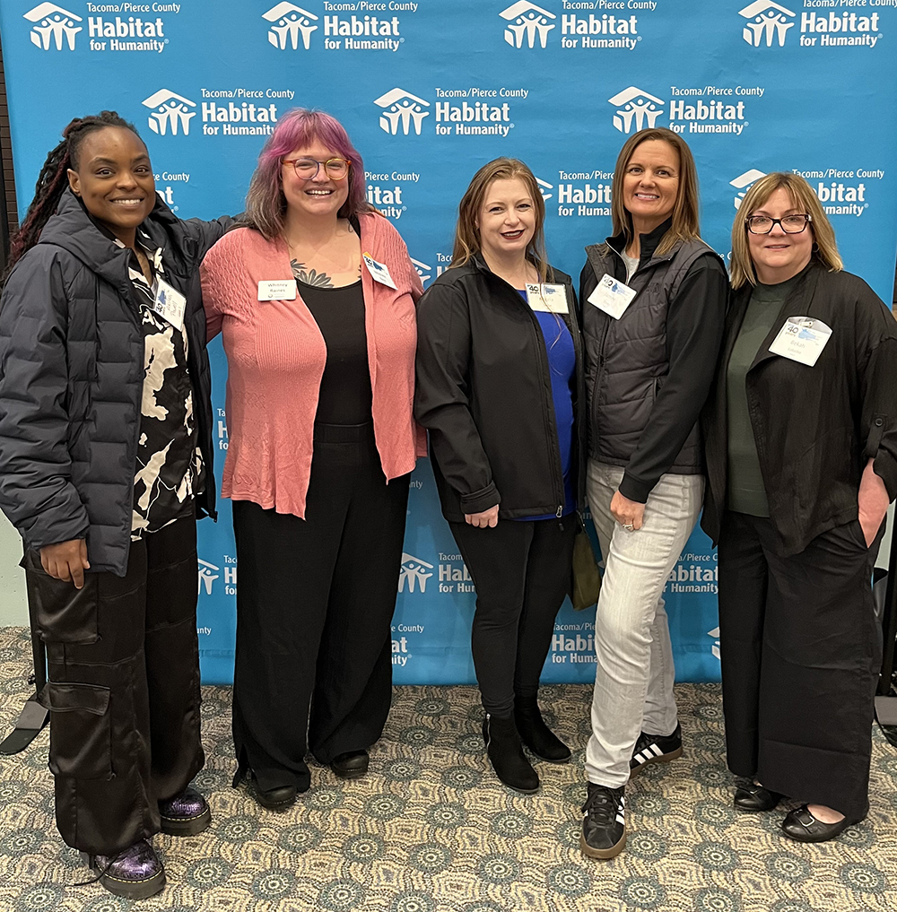 Five women in front of a Habitat for Humanity background.