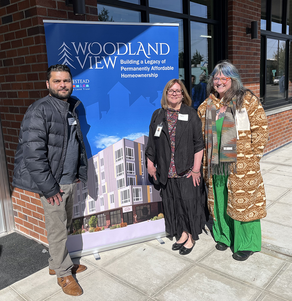 Three people pose at a banner for Woodland View affordable housing. 