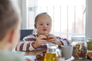 Photo of young girl with down syndrome eating sandwich at a table.