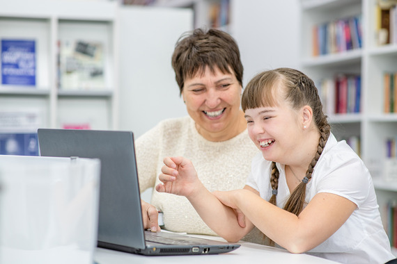Girl sitting next to her mother smiling at a computer