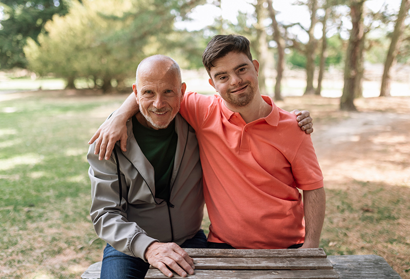 Happy senior father with his son with Down syndrome embracing and sitting in park.