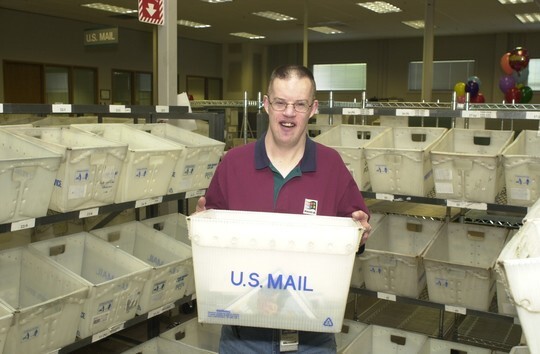 Dan Thompson smiling in the Microsoft mailroom holding a mail receptacle