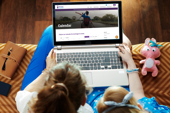 A caregiver and child look at the new Informing Families Community Calendar on a laptop, showing upcoming meetings and events