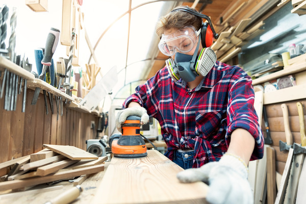 carpenter grinding raw wood with orbital sander tool