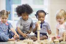 Four young children play together with wooden blocks on the floor.