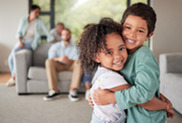 Children hugging with blurred family in background.