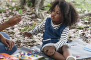 Child sitting on a blanket outdoors surrounded by fall leaves playing with colorful small toys working on fine motor skills. 