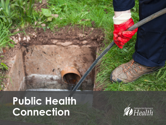 The foot and hand of a man is seen performing a maintenance task near a hole with access to a septic system.