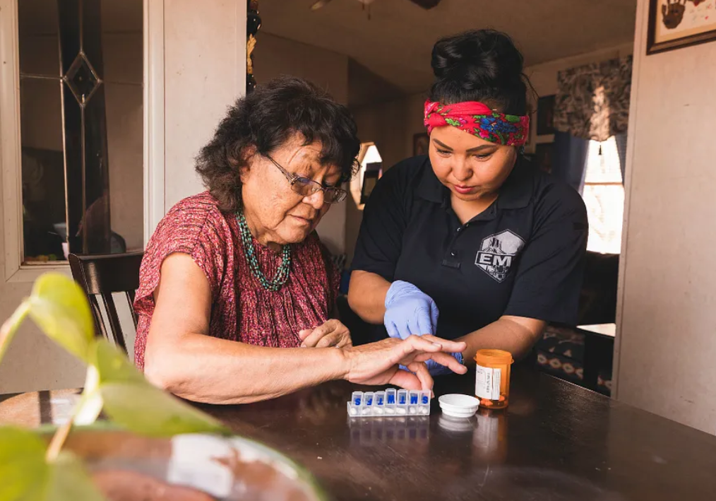 a health care worker helps a female patient sort her medications at a kitchen table