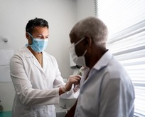 Female healthcare provider vaccinating senior Black man in doctor's office