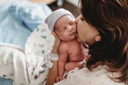 Mother kissing newborn baby in hospital bed.