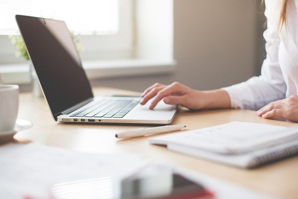 Woman navigating laptop on desk with pen and paper