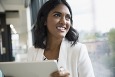 Smiling businesswoman with digital tablet looking out office window