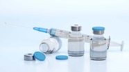 Syringe balanced on top of vial behind two full vials of clear liquid