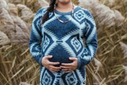 Pregnant woman in a blue patterned dress, holding belly, standing in long grass