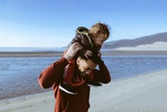 Father carrying son on shoulders near ocean
