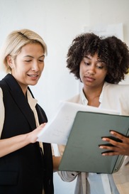 Two professional women reviewing papers in a binder