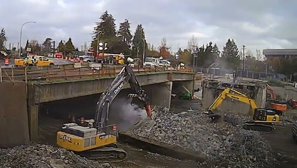 Two excavators remove large piles of rubble from the construction site of the 24th avenue overpass removal.