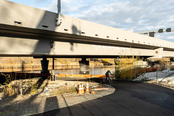 A bicyclist rides under a bridge on a bike trail.