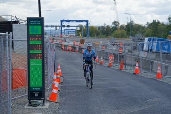 A bicyclist on a trail rides past a electronic counter.