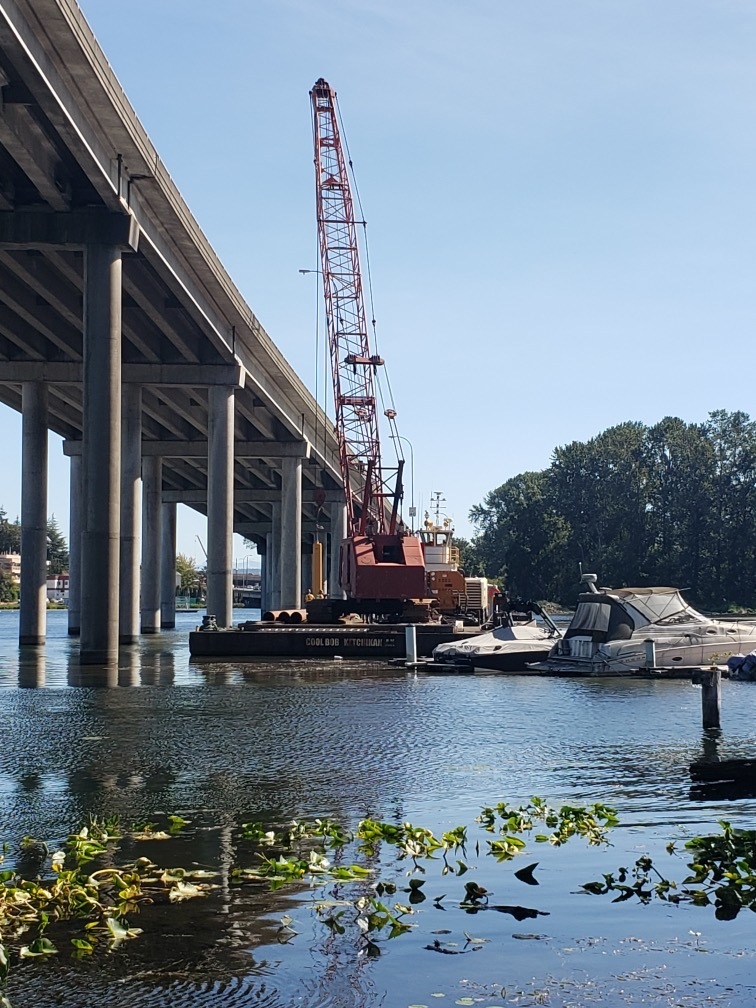 A crane is positioned on a barge as crews prepare to install a temporary test pile in Portage Bay. 