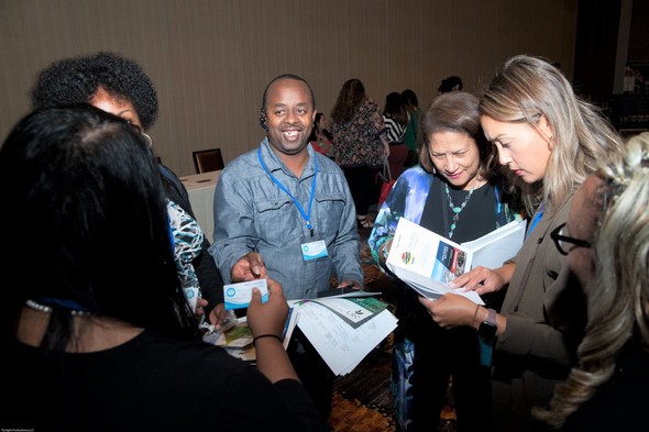 Photo shows an outreach event with a group of people standing, smiling and looking at materials