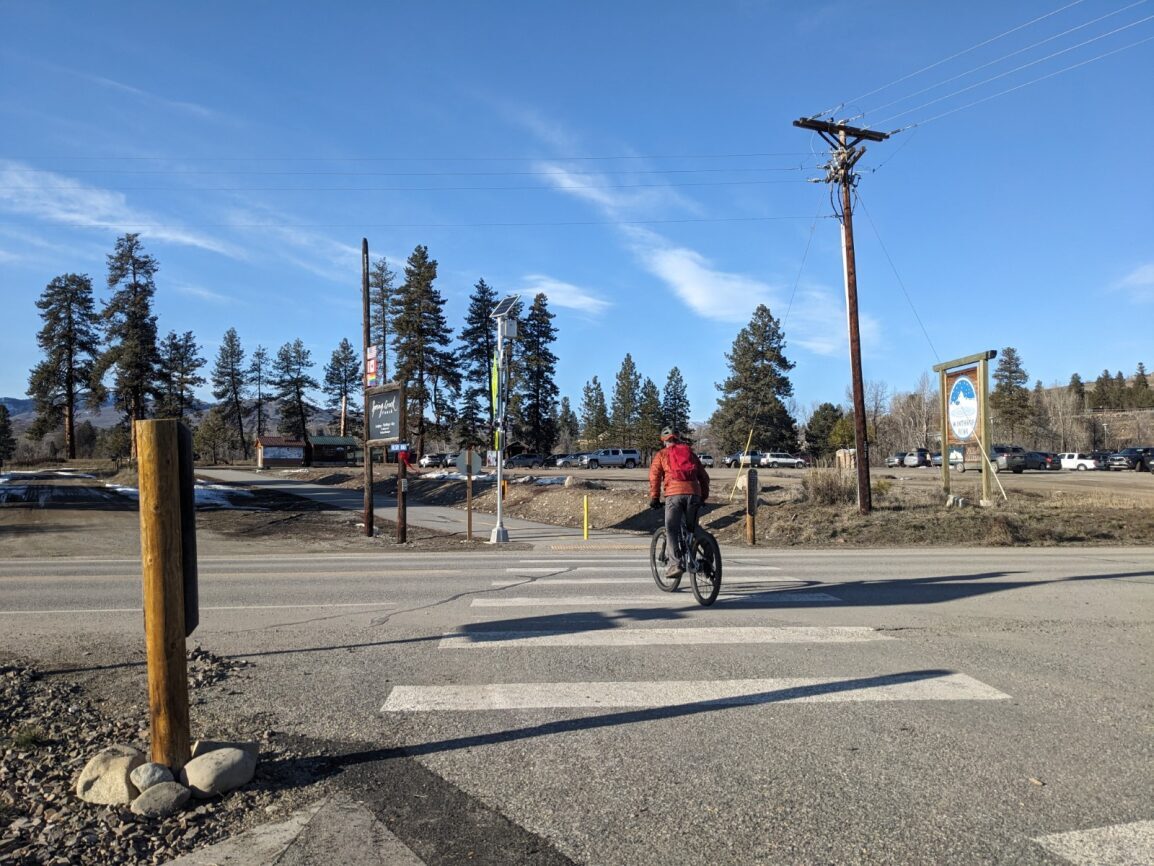A person on a bike crosses a street on a sunny day