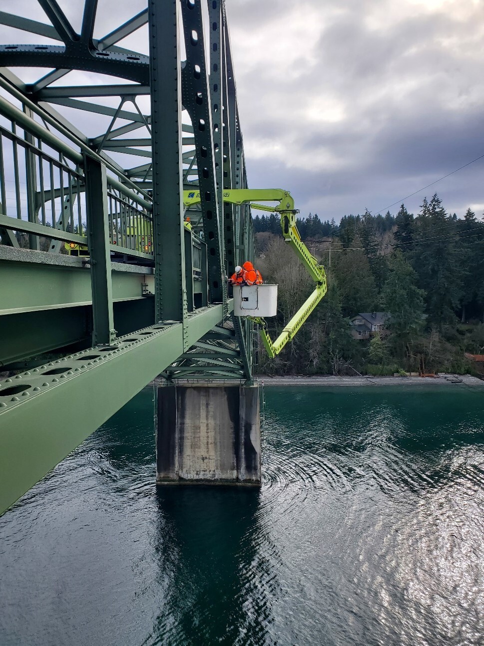 Photo of a green truck under green bridge over water in Portage Bay and maintenence workers in orange construction gear.jpg