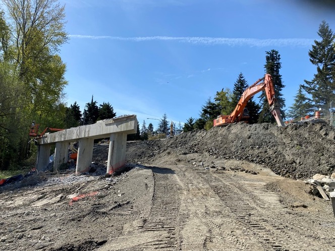 Photo shows ramp demolition with orange machinery on the right side, dirt on the ground, blue skies in background and structure on the left..jpg