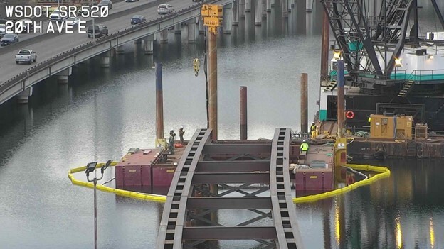 photo looking west shows foundations of a bridge an dbarge in the background of portage bay