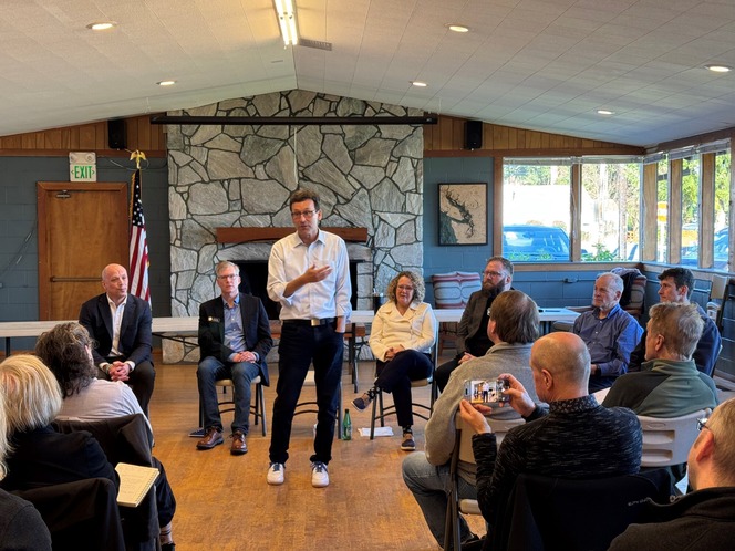 Gov.-elect Ferguson speaks to a group seated in a semi-circle in a room with a stone fireplace and large windows