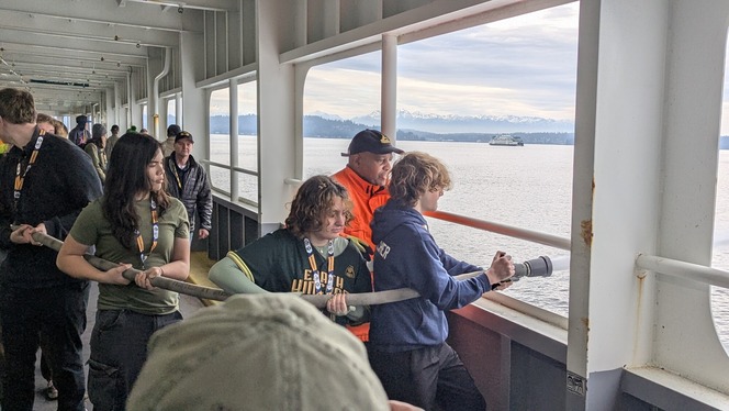 High School students operate a fire hose on the car deck of a ferry