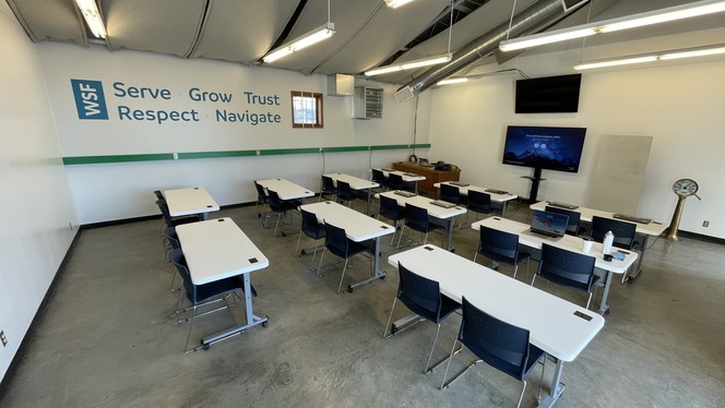 A modern classroom with white tables, blue chairs and large monitor and words "WSF, Serve, Grow, Trust, Respect and Navigate" on wall